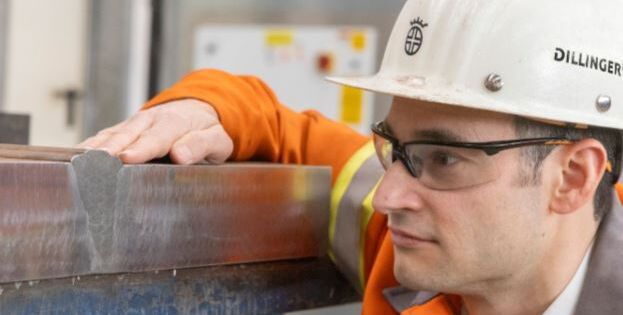Mann mit Schutzhelm und Schutzbrille schaut auf Stahlblock