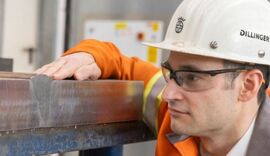 Mann mit Schutzhelm und Schutzbrille schaut auf Stahlblock